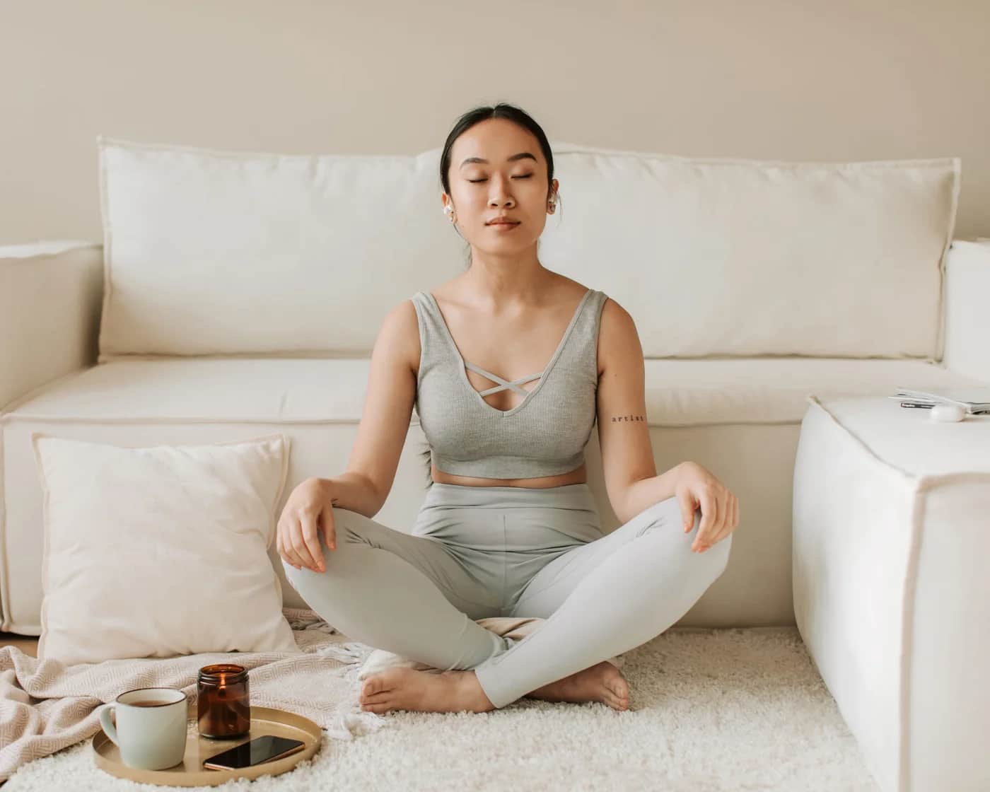A woman meditating calmly at home with a cup of tea and a candle