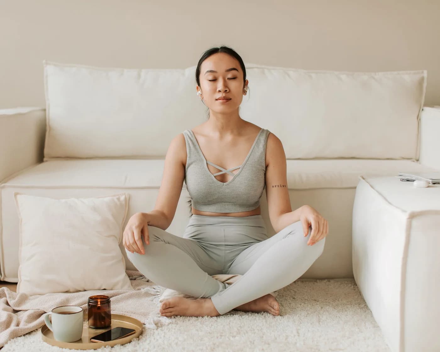 A woman meditating calmly at home with a cup of tea and a candle