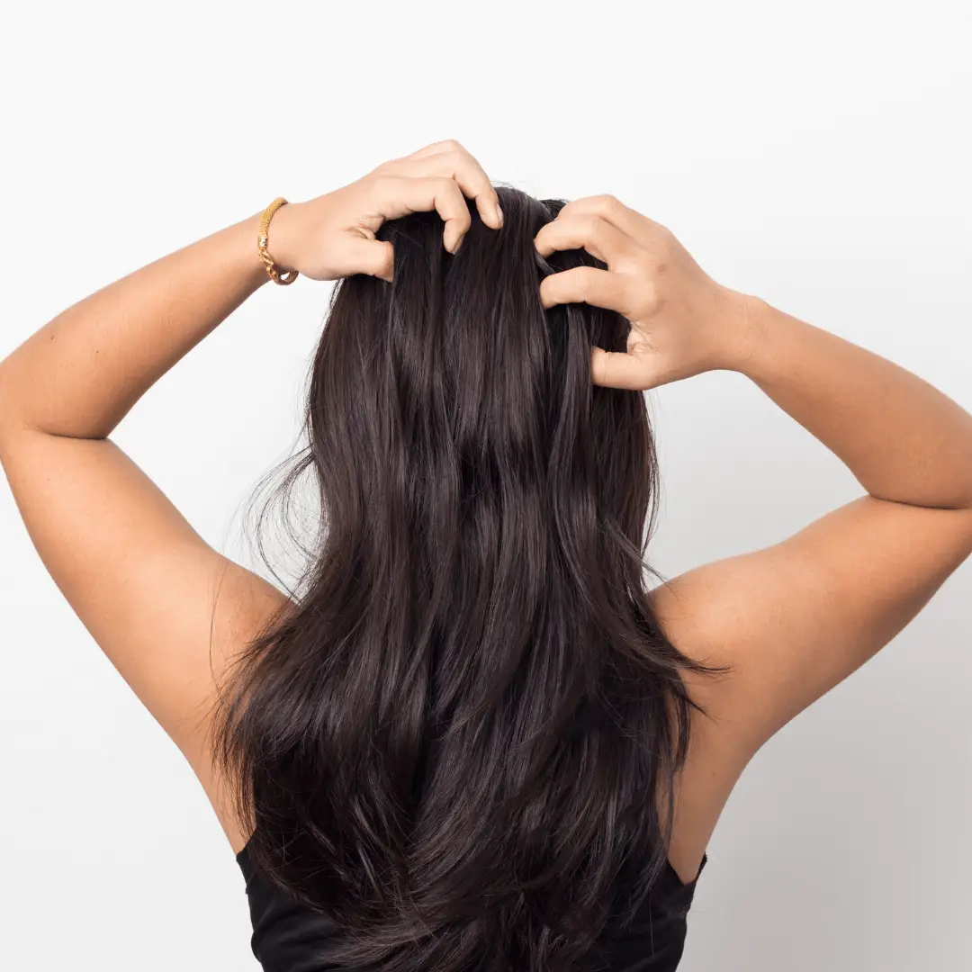 A woman with long dark hair combing her hair, demonstrating hair care essentials for a healthy scalp.