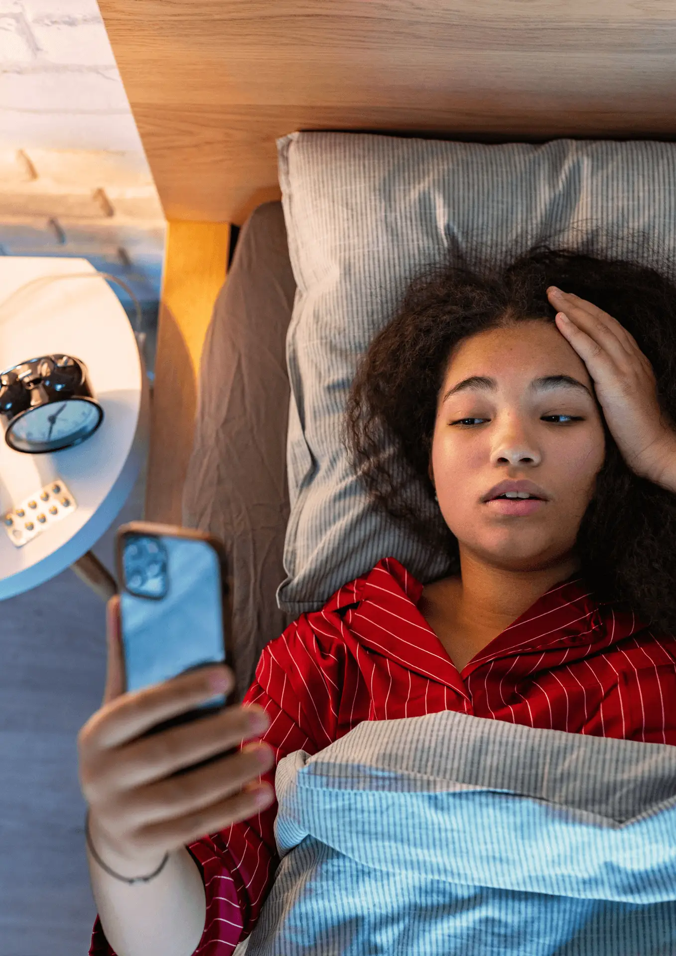 A woman laying in bed with her phone, looking stressed and unable to sleep.