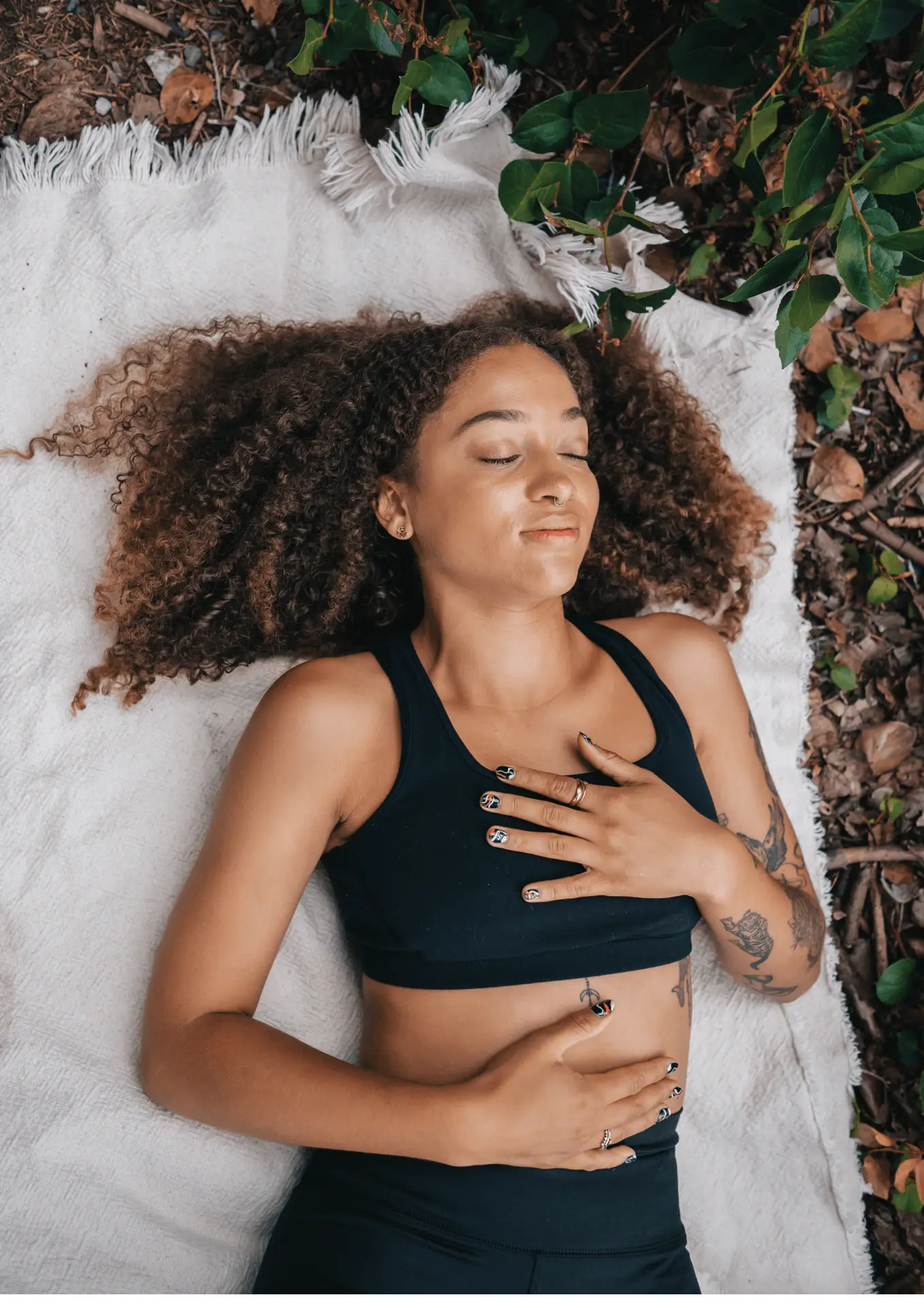 Woman laying on blanket with hands on stomach, practicing sleep meditation.