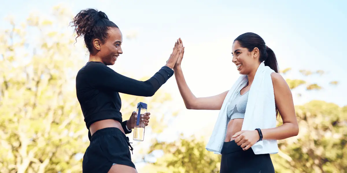 Two women high five while running in the park during the 30 day walking challenge