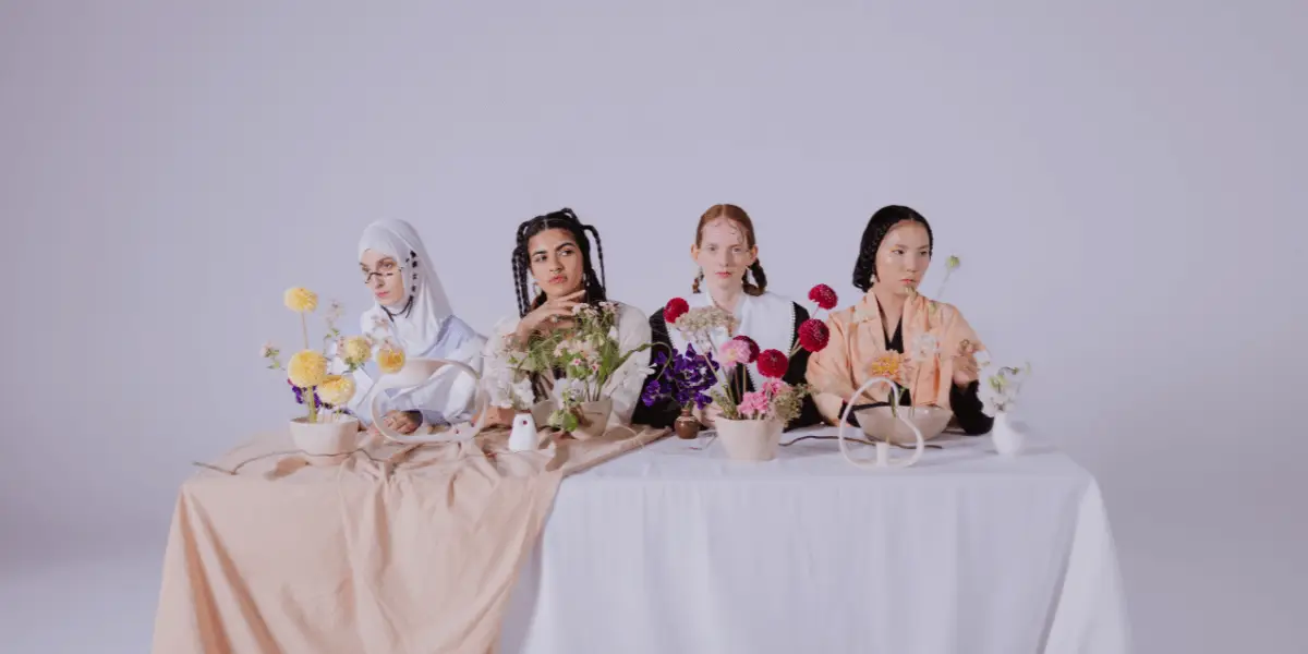 Five women sitting at a table adorned with flowers, representing diverse beauty ideals from around the world.