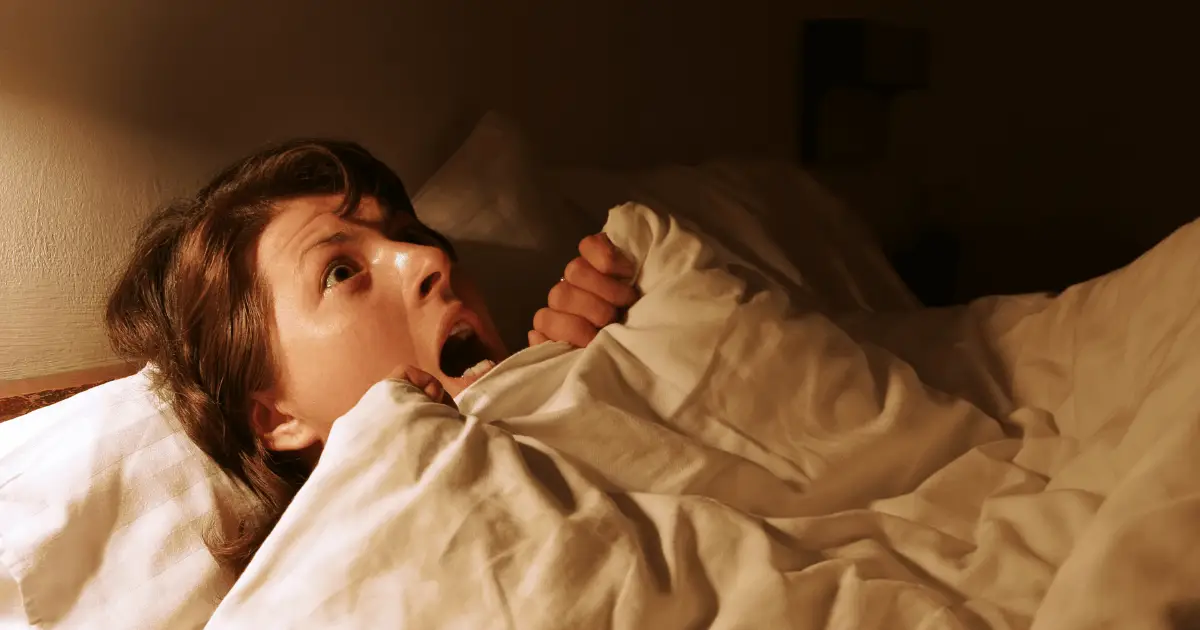 A woman sleeping in bed with her mouth open, having just woken up from a nightmare.