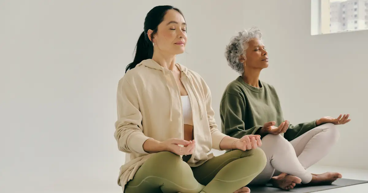 Two women practicing mindfulness meditation in a yoga studio.