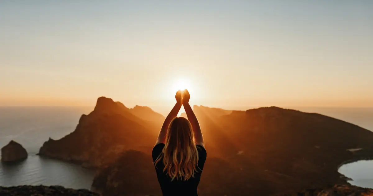 A woman standing on a mountain peak, arms raised, symbolizing Spiritual Awakening.