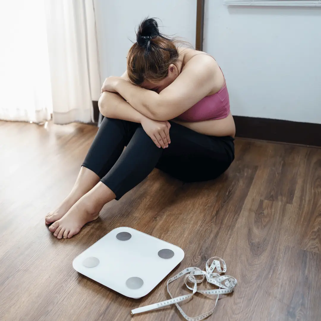 Female sitting on ground, weighing scale. weightloss is hard