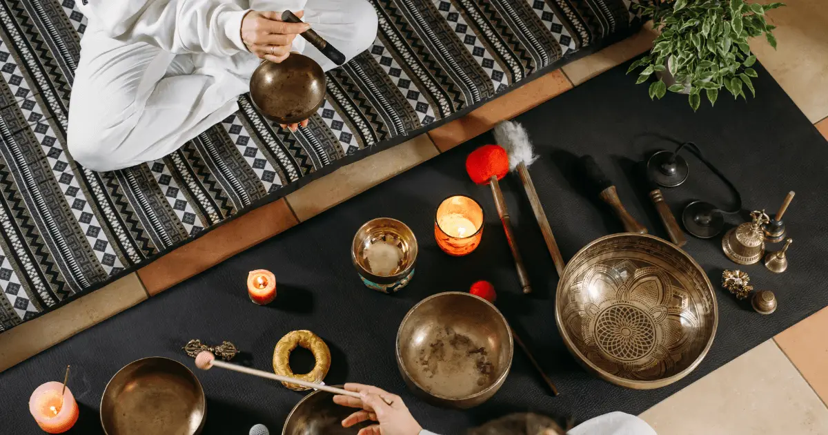 A person sits on a mat, surrounded by bowls, engaged in a sound bath meditation session.