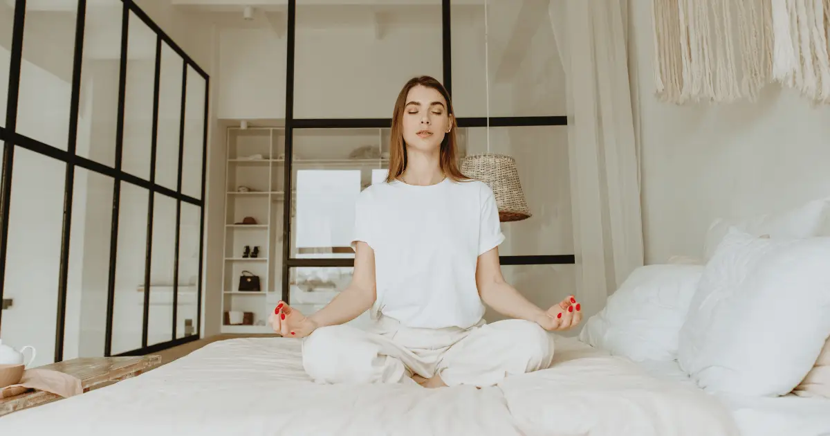 A woman peacefully meditating on her bed in a serene room, embracing the tranquility of morning meditation.