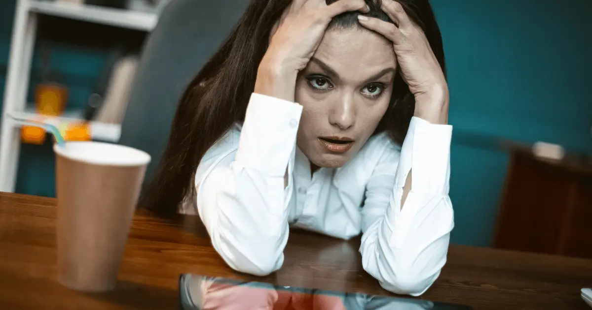 A woman at a desk, visibly stressed, with her head in her hands, reflecting the effects of high cortisol levels.