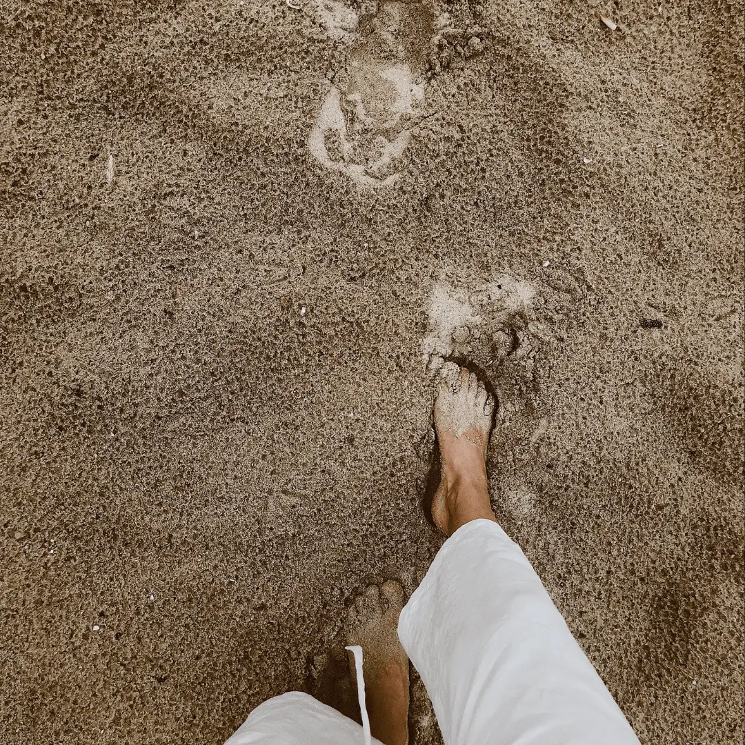 A person standing in the sand, engaging in a grounding exercise by connecting with the earth
