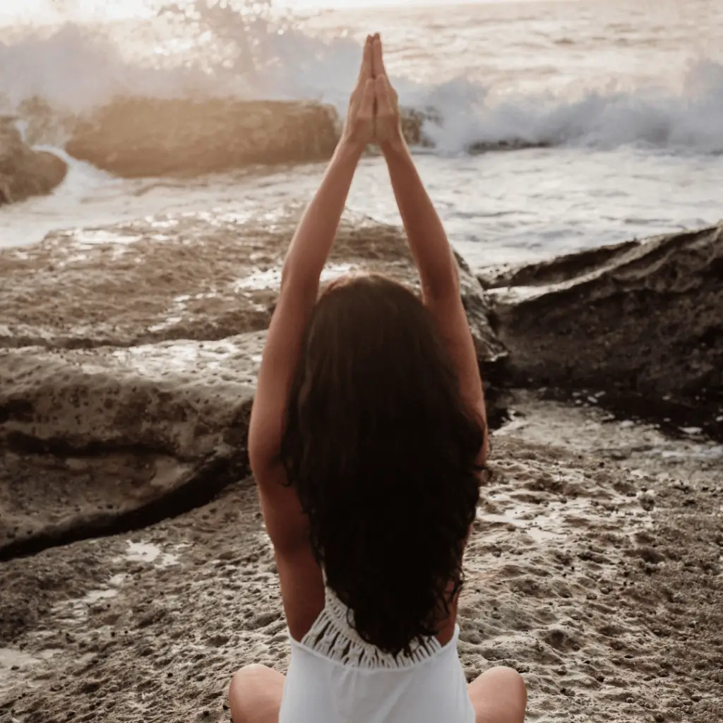 A tranquil scene of a woman in a white dress doing yoga on the beach, emphasizing grounding exercises and deep breathing