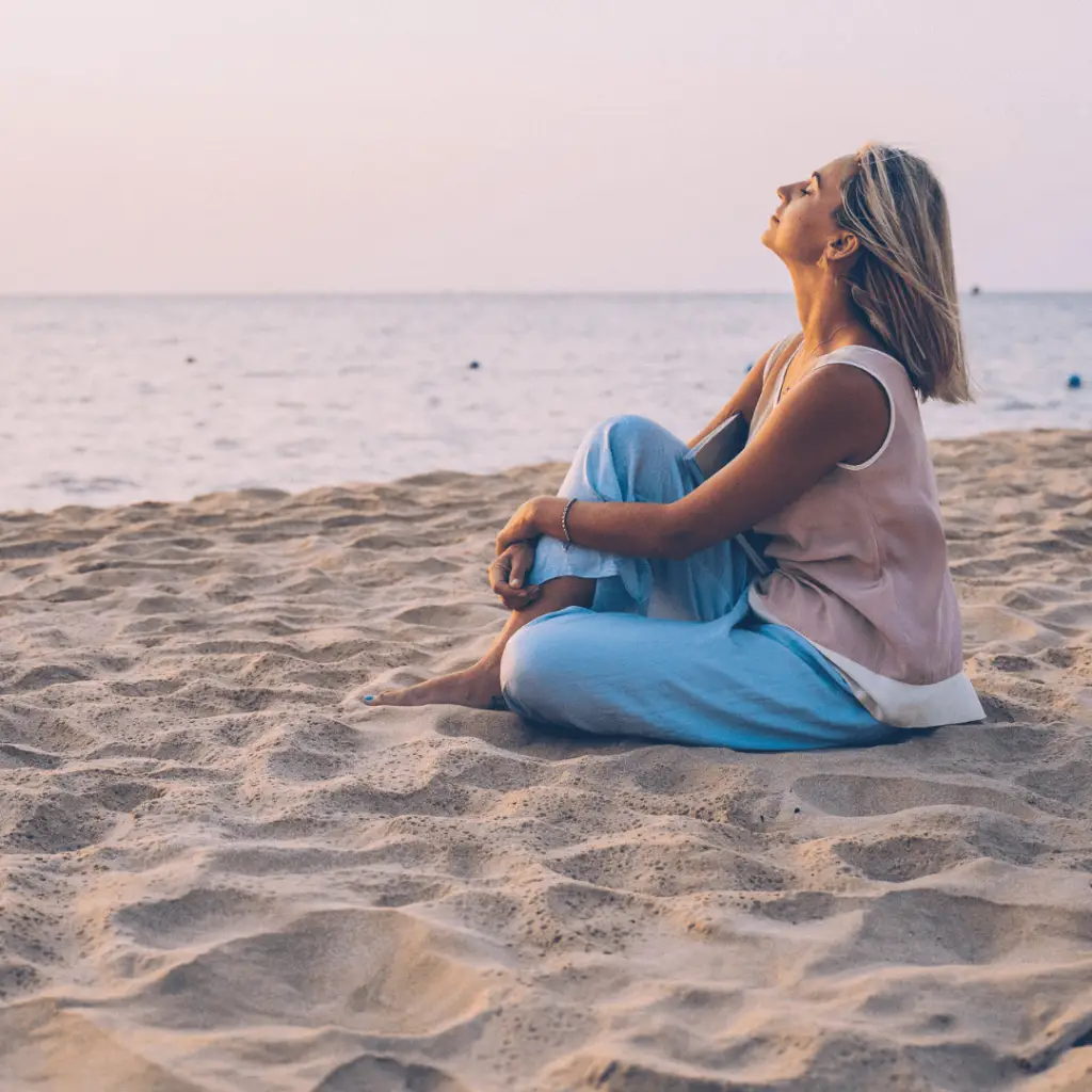 Beach scene_ woman sitting with eyes closed, practicing grounding exercise