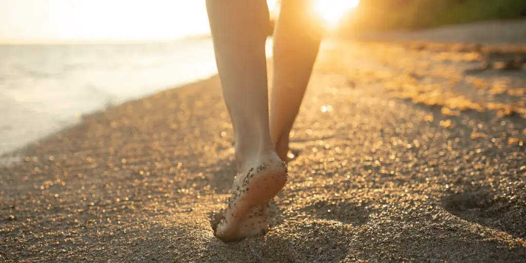 Sunset beach stroll, person practicing grounding exercise by walking