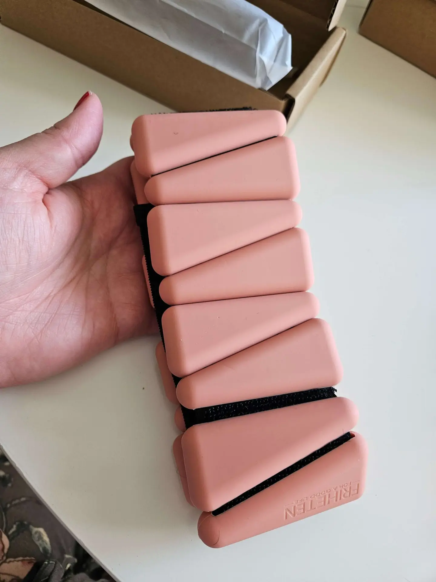 A hand holding a pink case with various shapes inside, used as an ankle weight.