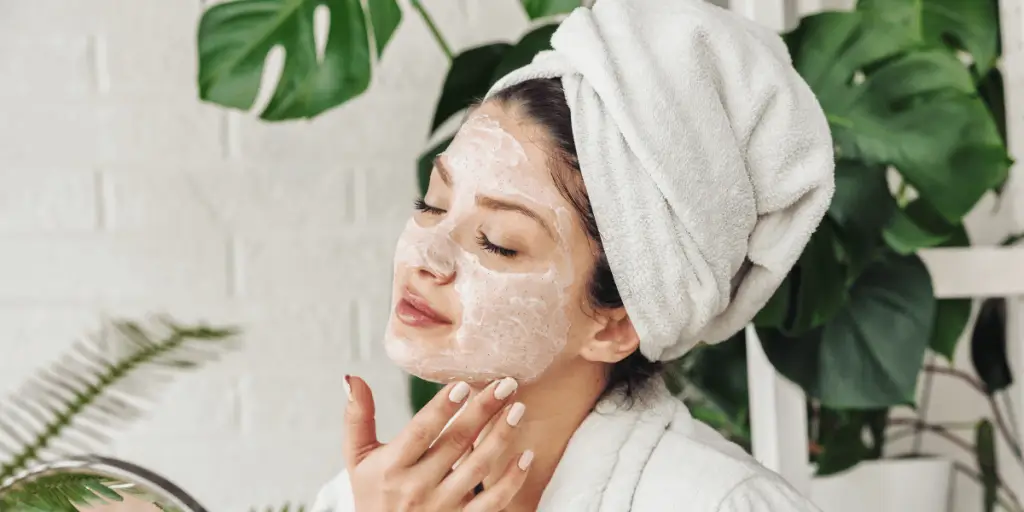 A woman with a face mask and towel on her head, showcasing celebrity beauty secrets in skincare.