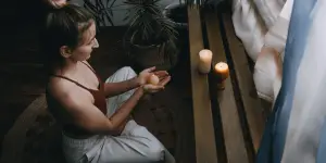 The picture depicts a woman sitting on the floor, holding a candle, while connecting to her higher self.