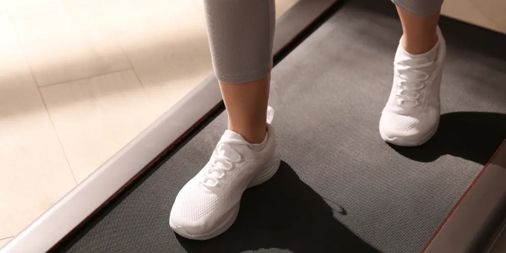 Woman in white sneakers walking on treadmill for indoor walking challenge.