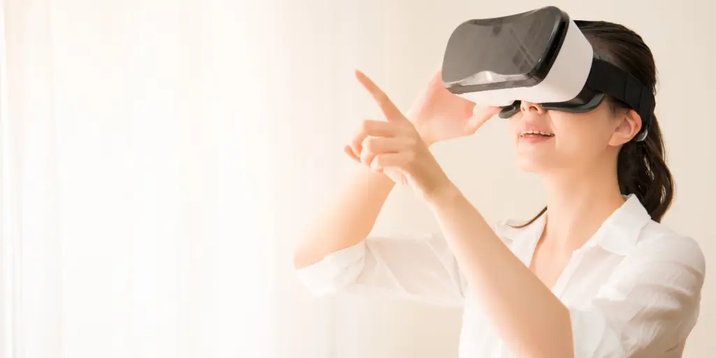 A woman in a white shirt holds a virtual reality headset. She is likely exploring Games for Health using Augmented Reality technology.