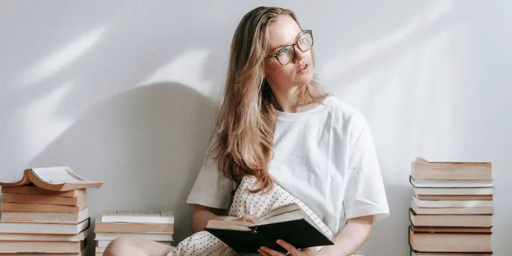 A woman in glasses sits on the floor with a book, engaging in mental exercises.