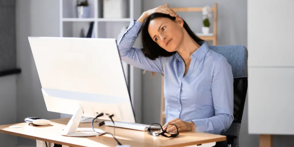 A woman sitting at a desk with her head in her hands, demonstrating exercises for a busy lifestyle at work.