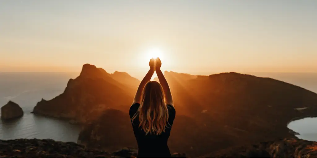 A woman triumphantly stands atop a mountain, her hands raised high in the air, symbolizing victory and a sense of accomplishment. The image conveys the message of Protect energy.