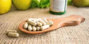A wooden spoon filled with immune-boosting pills and green apples, natural supplements for a healthy lifestyle.