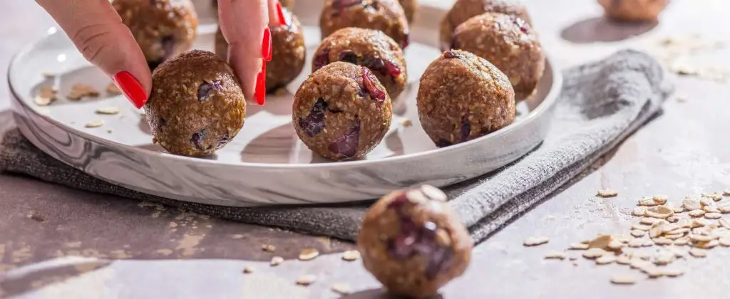 A plate of oatmeal energy balls with a woman's hand reaching for them.