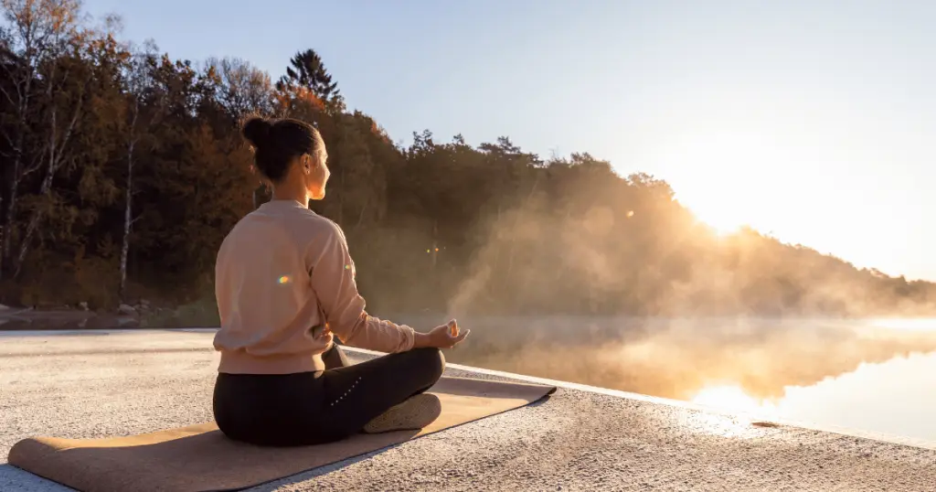 Woman meditating in yoga pose by lake, practicing 5-minute mindfulness meditation.