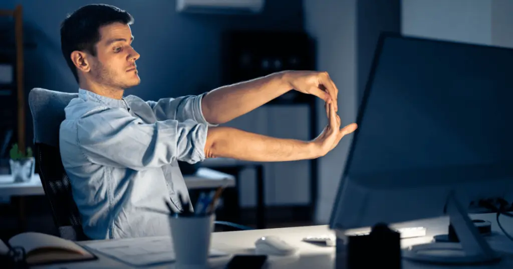 A man sitting at a desk with his hands raised in a desk yoga pose.