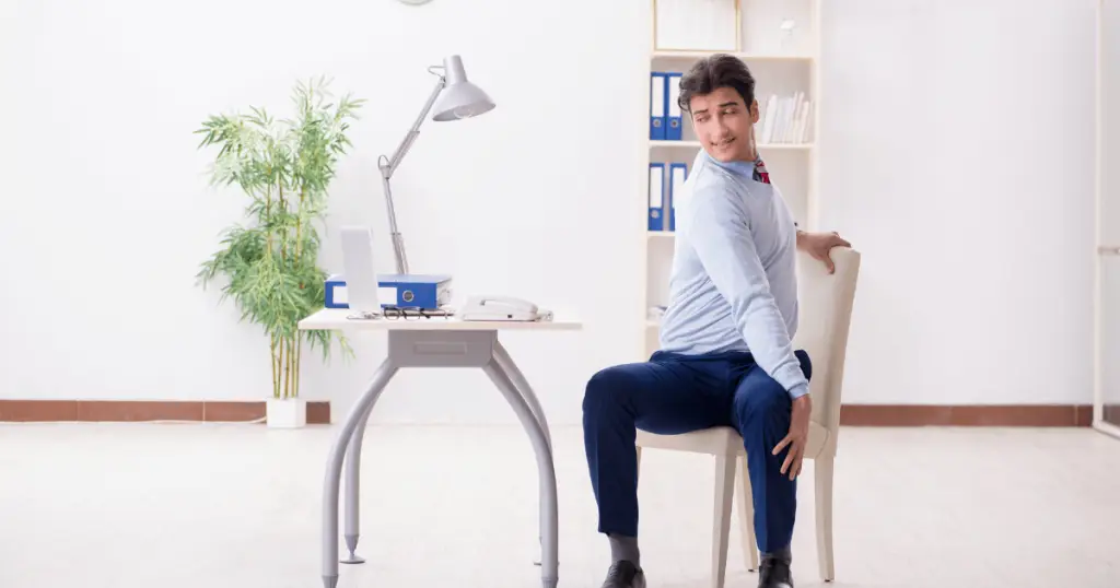A man practicing desk yoga, seated on a chair in front of a desk, promoting relaxation and well-being in the workplace.