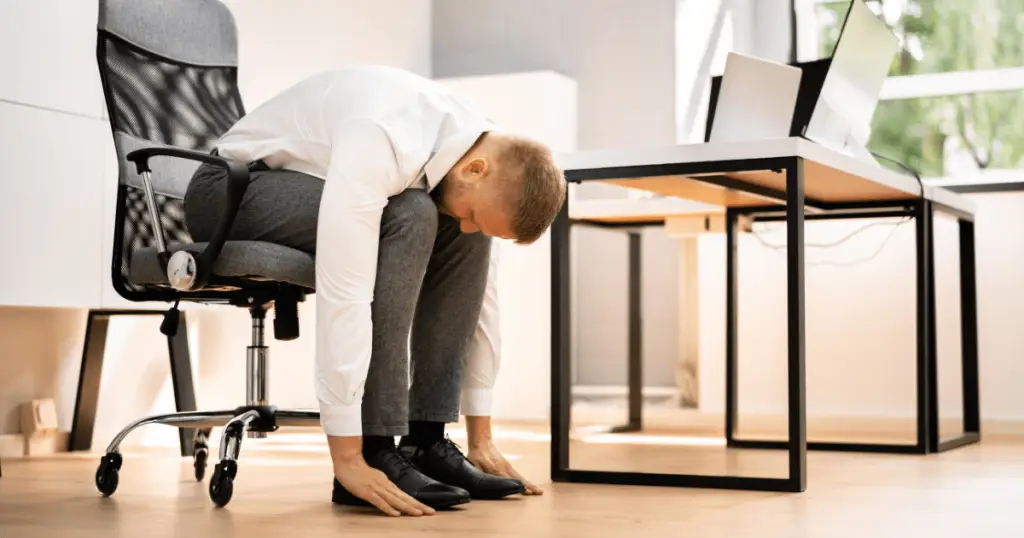 A man sitting on a chair with legs up, practicing desk yoga.