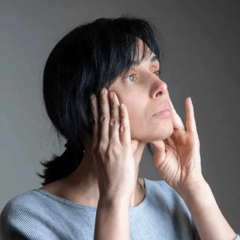 A woman practicing facial yoga, gently touching her face with her hands to enhance relaxation and rejuvenation.