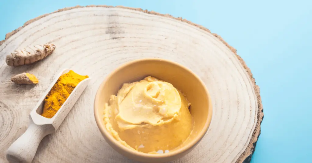 A bowl of turmeric paste sits on a wooden plate, highlighting its use in DIY beauty hacks and natural skincare remedies.