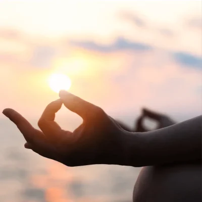 A person meditating with the sunset in the background, strengthening connection with their higher self through meditation.