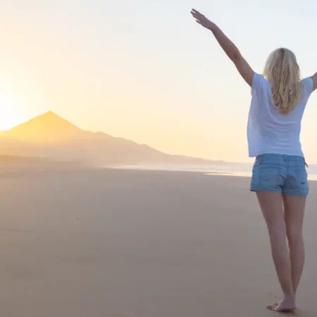 A woman on the beach with arms outstretched, embodying her higher self and living a fulfilling life.