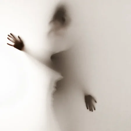 A woman with outstretched hands stands in front of a wall, embodying the concept of shadow work and the quest for self-understanding.